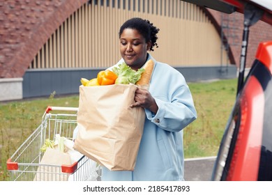 Waist Up Portrait Of Young Black Woman Putting Grocery Bag In Car Trunk At Supermarket Parking Lot