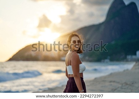 waist up portrait young brazilian cheerful smiling woman on ipanema beach looking over her shoulder at the camera at sunset