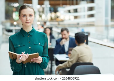 Waist Up Portrait Of Young Businesswoman Holding Planner And Looking At Camera In Office Building Interior, Copy Space