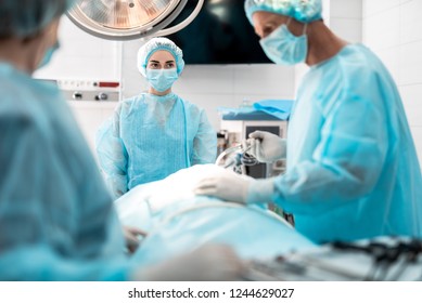 방호마스크와 살균된 가운을 입은 젊은 여성의 초상화를 허리띠로 감고 의사가 어떻게 수술을 하는지 지켜보아요 스톡 사진