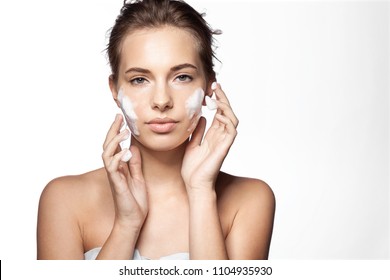 Waist up portrait of young pretty woman applying foaming cleanser. Lovely female with clean fresh perfect skin looking at camera with calmness. Skincare concept. Isolated on white background