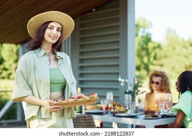 Waist Up Portrait Of Young Woman Holding Tray Of Snacks Looking At Camera While Enjoying Outdoor Party With Friends In Summer, Copy Space