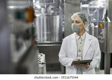 Waist up portrait of young woman wearing mask and holding digital tablet during quality control inspection at food factory, copy space - Powered by Shutterstock