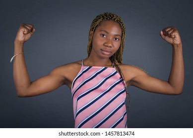 Waist Up Shot Of African American Woman Woman Raises Arms To Show Her Muscles Feels Confident In Victory, Looks Strong And Independent, Smiles Positively At Camera, Stands Against Gray Background. Spo