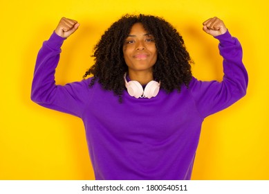 Waist Up Shot Of African American Woman Raises Arms To Show Her Muscles Feels Confident In Victory, Looks Strong And Independent, Smiles Positively At Camera, Stands Against Gray Background. Sporty.