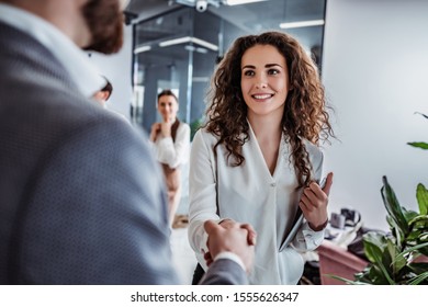 Waist up shot of beautiful young woman shaking hand to stylish businessman in office setting - Powered by Shutterstock