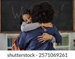 Waist up shot of teenage African American girl embracing teacher in classroom and smiling happily with blackboard in background, copy space