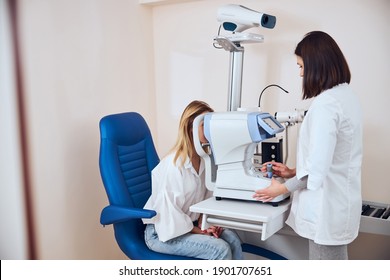 Waist up side view portrait of brunette female doctor working with ophthalmoscope while examining vision of blonde Caucasian patient in optician clinic - Powered by Shutterstock