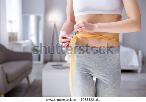 Waist size. Nice slim woman holding a centimeter\
tape while measuring her\
waist