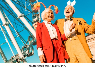 Waist Up Of Smiling Elderly Couple Having Fun While Standing Near Ferris Wheel