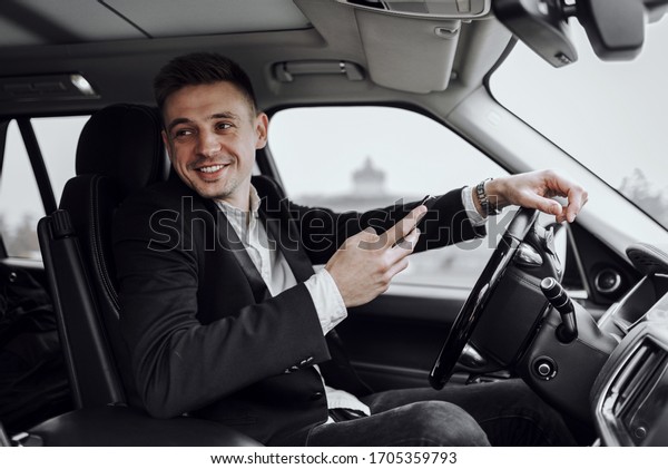 Waist up of smiling handsome\
man renting automobile and using smartphone. Rent and trade-in\
concept