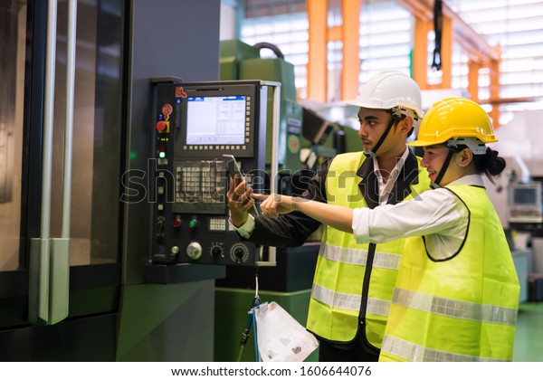 Waist up two Asian factory engineer and\
inspector with safety helmet check render productivity in digital\
tablet at robot machine monitor. Manufacturing industry to produce\
car parts. Quality\
control.