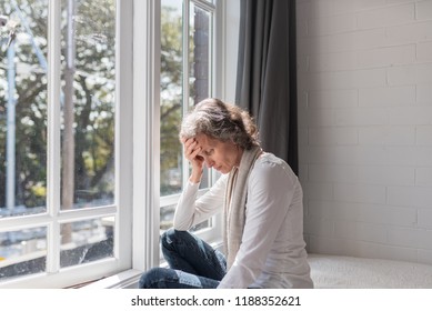 Waist up view of middle aged woman sitting by window resting head on her hand (selective focus)