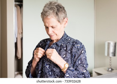 Waist Up View Of Older Woman Doing Up Buttons On Blue Blouse While Getting Dressed In Bedroom (selective Focus)