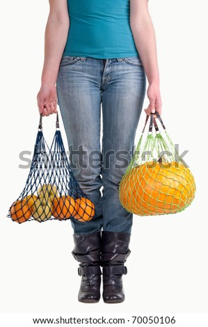 Waist-down view of young woman carrying string shopping bags (Einkaufsnetz) with yellow fruits (pumpkin, apples, lemons, oranges) isolated on white background