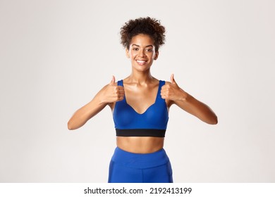 Waist-up Of Beautiful African-american Fitness Woman, Wearing Blue Sport Outfit, Showing Thumbs-up In Approval, Recommend Gear For Workout, White Background