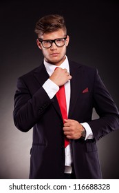 waist-up picture of a young business man fixing his tie and looking into the camera. on dark background