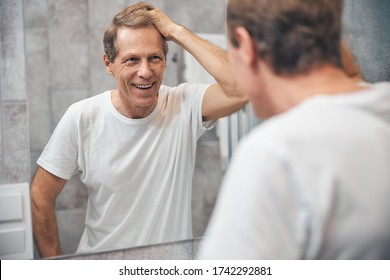 Waist-up Portrait Of An Attractive Pleased Middle-aged Caucasian Man Touching His Hair With A Hand