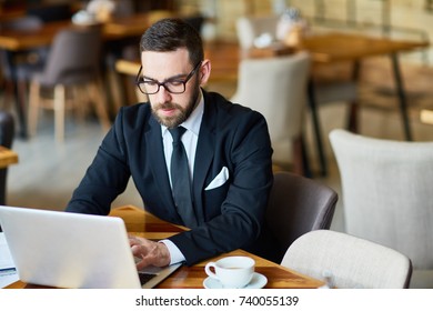 Waist-up portrait of confident financial manager preparing annual accounts with help of laptop while working at spacious restaurant