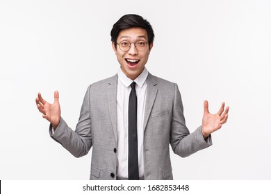 Waist-up Portrait Of Excited, Happy Young Lucky Asian Man In Grey Suit, Describe Something Big, Stretch Hands Sideways And Smiling Amazed, Talking About Fantastic Promo Offer, White Background