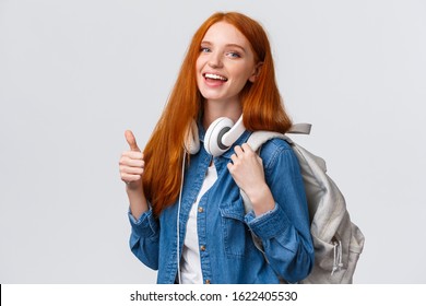 Waist-up portrait joyful cute redhead girl inviting freshmen apply univeristy, got scholarship, smiling showing thumbs-up in approval, recommendation, holding backpack and headphones - Powered by Shutterstock