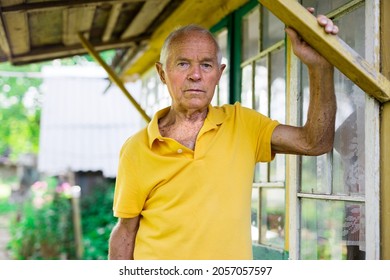 Waist-up portrait of old man standing on porch of his country house.