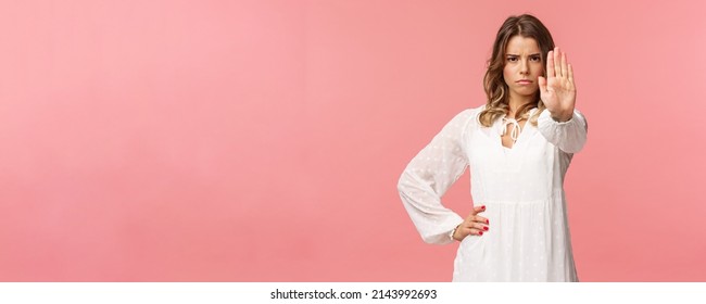 Waist-up portrait of serious-looking assertive and confident young blond female in white dress, extend arm in stop motion, frowning, demand quit, prohibit something, warning express disagreement - Shutterstock ID 2143992693