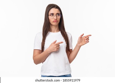 Waist-up Portrait Of Skeptical And Restrained Young Brunette Pretty Woman Staying Away From Suspicious Person, Peeking And Pointing Right With Disapproval Look, Hesitating, Judging Someone