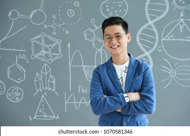 Waist-up portrait of smiling teenage student wearing eyeglasses posing for photography with arms crossed while standing against blackboard - Powered by Shutterstock