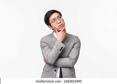 Waist-up Portrait Of Thoughtful, Creative And Smart Asian Young Man In Grey Suit, Office Manager, Businessman Planning Project, Thinking Looking Up Pondering Ideas, White Background