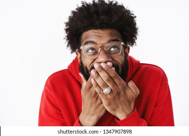 Waist-up shot of delighted happy african american male bearded friend in glasses chuckling, giggling with hand covering mouth looking up amused awaiting for prank come in action, joking over friend