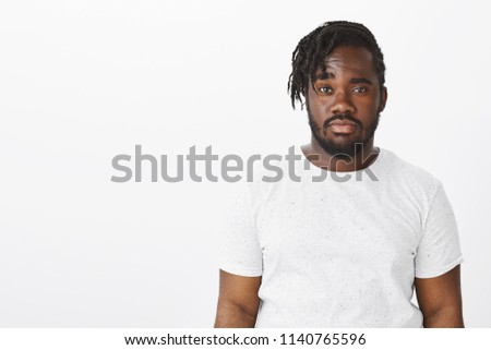 Waist-up shot of doubtful unimpressed dark-skinned man with stylish haircut, raising one eyebrown with doubt and staring seriously at camera, being careless and indifferent over white background