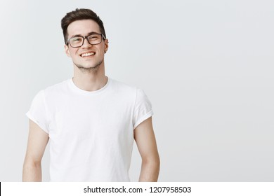 Waist-up shot of pleasant and friendly-looking handsome happy young guy in glasses smiling broadly as standing over gray copy space carefree and joyful living fulfilled life, enjoying conversation - Shutterstock ID 1207958503