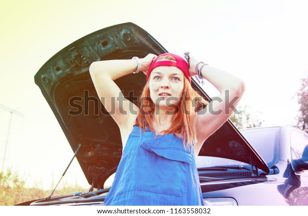 Wait for roadside\
assistance. Portrait of a young woman standing next to her car in\
panic and open car hood.