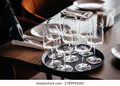 Waiter arranging table setting with empty wine glasses and cutlery in elegant restaurant interior. Hospitality preparation and fine dining service concept.