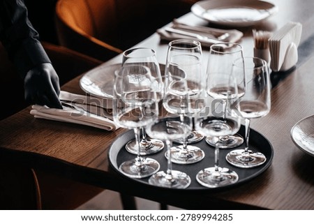 Waiter arranging table setting with empty wine glasses and cutlery in elegant restaurant interior. Hospitality preparation and fine dining service concept.