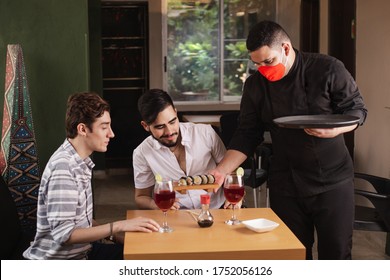 Waiter With Biosecurity Measures In Times Of Coronavirus. Person Serving Sushi In A Reopened Restaurant