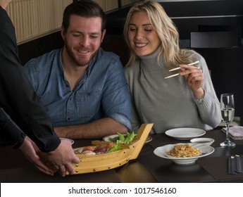 Waiter Bring The Sushi Roll Boat To A Couple In Restaurant