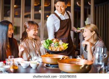 waiter  bring  vegetables for hot pot  and serving group of friends in restaurant