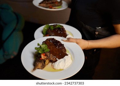 Waiter carrying two plates with meat dish on some festive event, party, wedding reception or catered event
