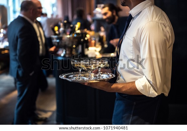Waiter from catering service carrying champagne\
wine drinks on the event