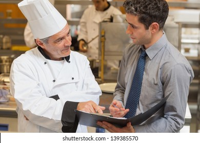 Waiter and chef discussing the menu in the kitchen - Powered by Shutterstock