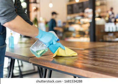 Waiter cleaning table with disinfectant spray and Microfiber cloth in cafe covid-19 preventing.
