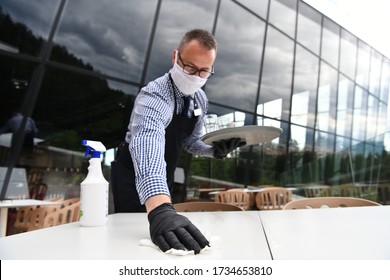 Waiter cleaning the table with Disinfectant Spray in a restaurant wearing protective medical mask and gloves new normal concept