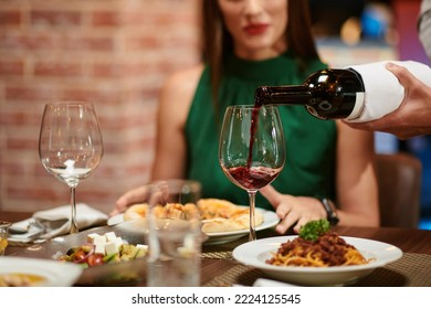 Waiter filling wine glass for yuong elegant woman sitting at restaurant table - Powered by Shutterstock