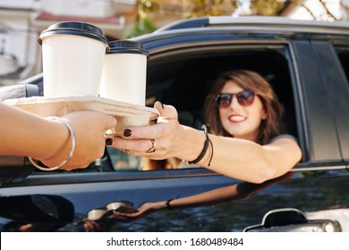 Waiter giving disposable tray with two cups of take out coffee to pretty smiling female driver