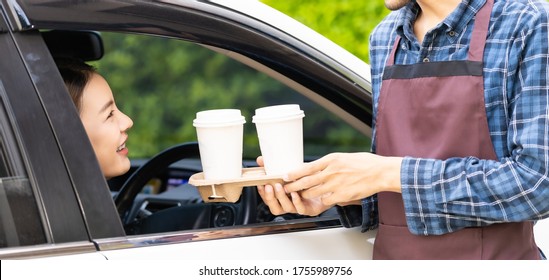 Waiter giving hot coffee cup disposable tray and bakery bag through car window to customer at drive thru service station. Drive thru is popular service after coronavirus covid-19 pandemic. Panoramic.