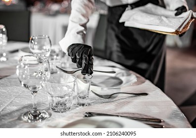 waiter hand in gloves puts the knife and fork, table setting