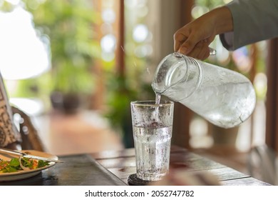 Waiter hand pouring water with ice into glasses on table