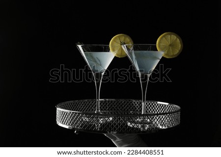 Waiter holding elegant tray with martini glasses of fresh cocktail against black background, closeup